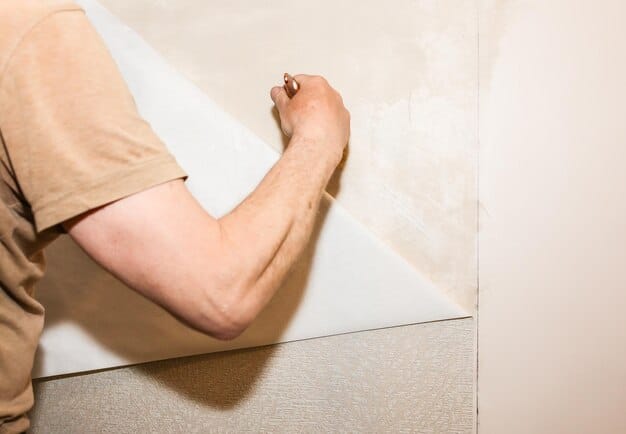 A close-up shot of a person tiling a bathroom wall in a herringbone pattern. The person is wearing gloves and using a trowel to apply adhesive.