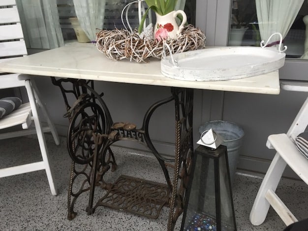 A close-up of a repurposed vintage sewing machine table being used as a bathroom vanity. The original iron base is intact, and a modern sink and faucet are installed on top, blending rustic and contemporary styles.