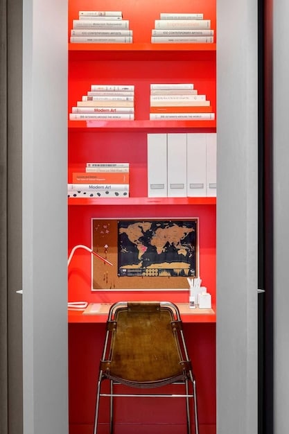 A small home office nook with a wall-mounted desk and custom-built shelving reaching up to the ceiling. The shelves are filled with books, plants, and decorative items, creating an organized and visually appealing workspace.