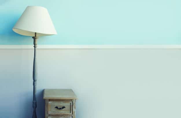 A close-up of a bedroom wall painted in a soft, light blue, with a white bedside table and a small lamp, highlighting the calming effect of the color.