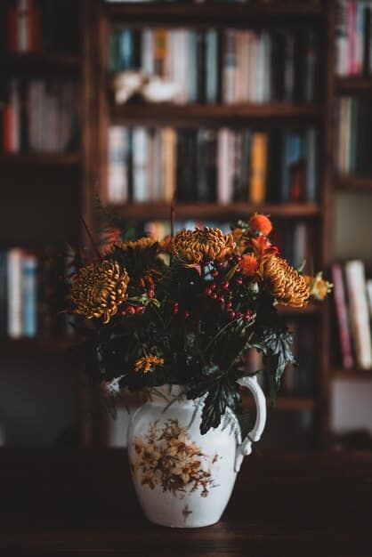 A close-up shot of a curated bookshelf with a mix of books, decorative vases, small sculptures, and framed photos. The arrangement is artistic and intentional, showcasing different textures and heights. The lighting highlights the details and creates a warm, inviting atmosphere.