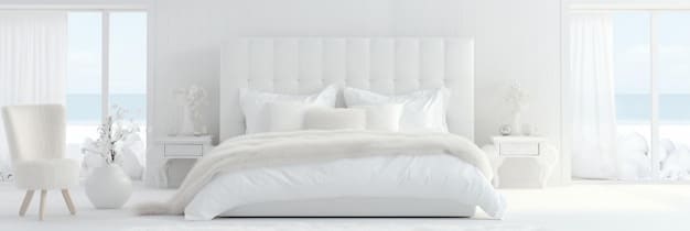 A minimalist bedroom featuring a white platform bed with crisp white linens. A single piece of art hangs above the bed, and a potted plant sits on a simple nightstand. Natural light streams in through a large window, highlighting the clean lines and clutter-free surfaces.