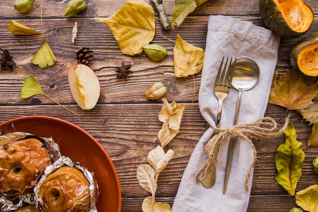 A dining table set for a fall-themed dinner, featuring a burlap table runner, rustic wooden chargers, and earthenware plates. Autumn leaves and small gourds are scattered as decorative accents.